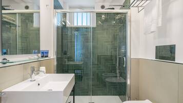 A modern bathroom with a glass-enclosed shower, a white sink, and a toilet.