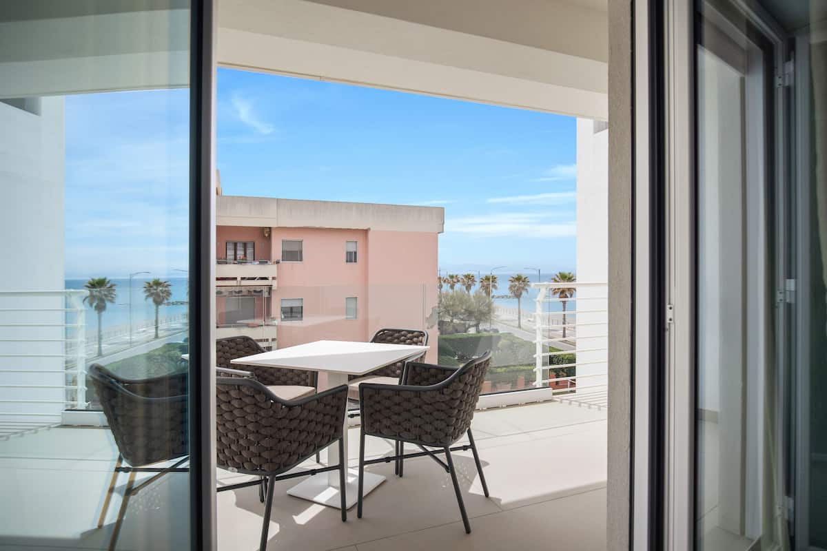 A balcony with a table and chairs, overlooking a building and palm trees.