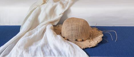 A bed with a blue headboard, two floral pillows, a straw hat, and a white throw blanket.