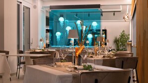 A modern dining area with tables set for a meal, ambient lighting, and a view of the cityscape through a glass wall. - Seaside Hotel (Capo d'Orlando)