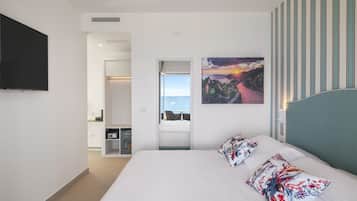 Habitación de hotel moderna con una cama grande, un televisor de pantalla plana en la pared, un cuadro de un atardecer y vistas a través de una puerta abierta.