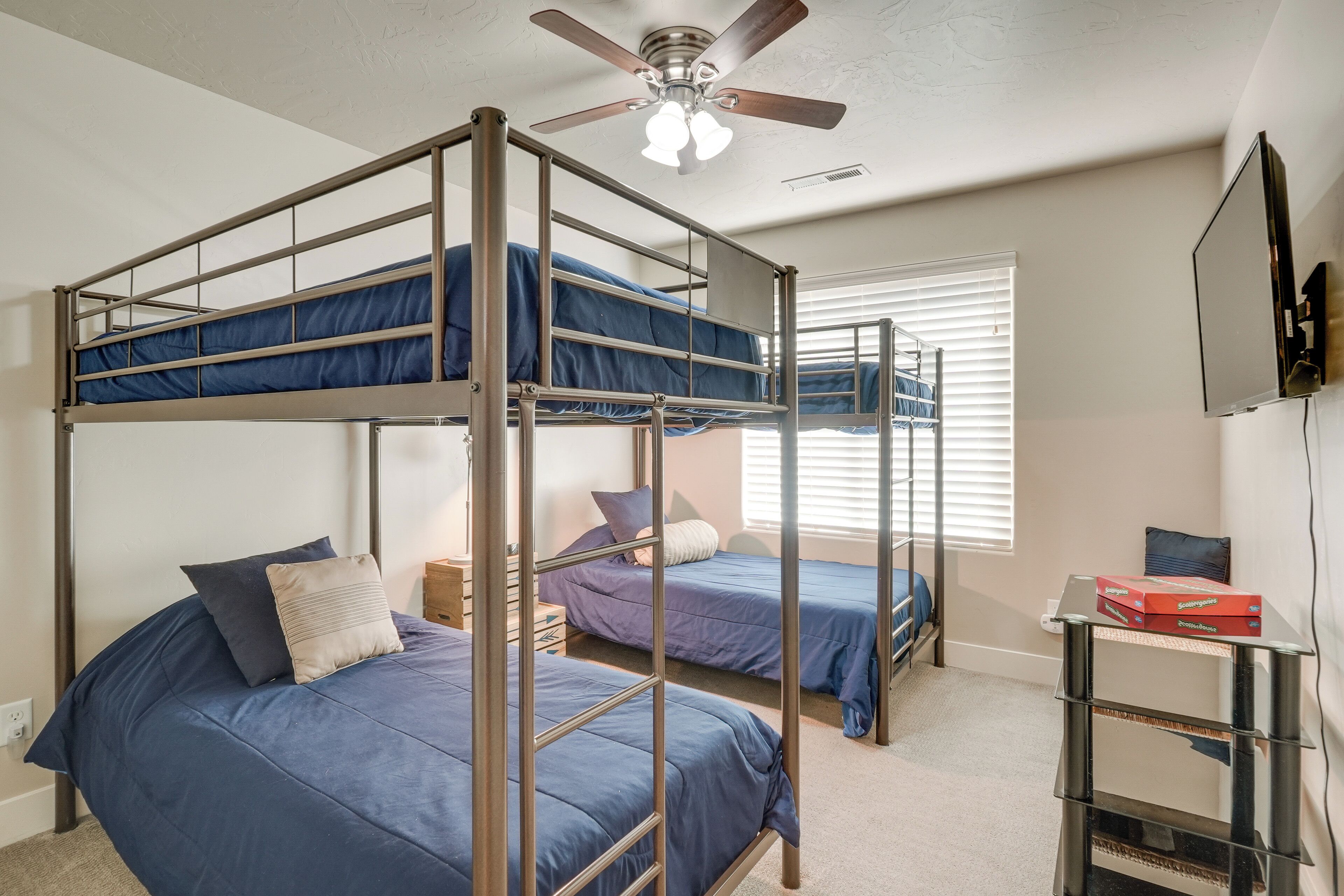 A bunk bed room with a ceiling fan, a TV, and a window with blinds.