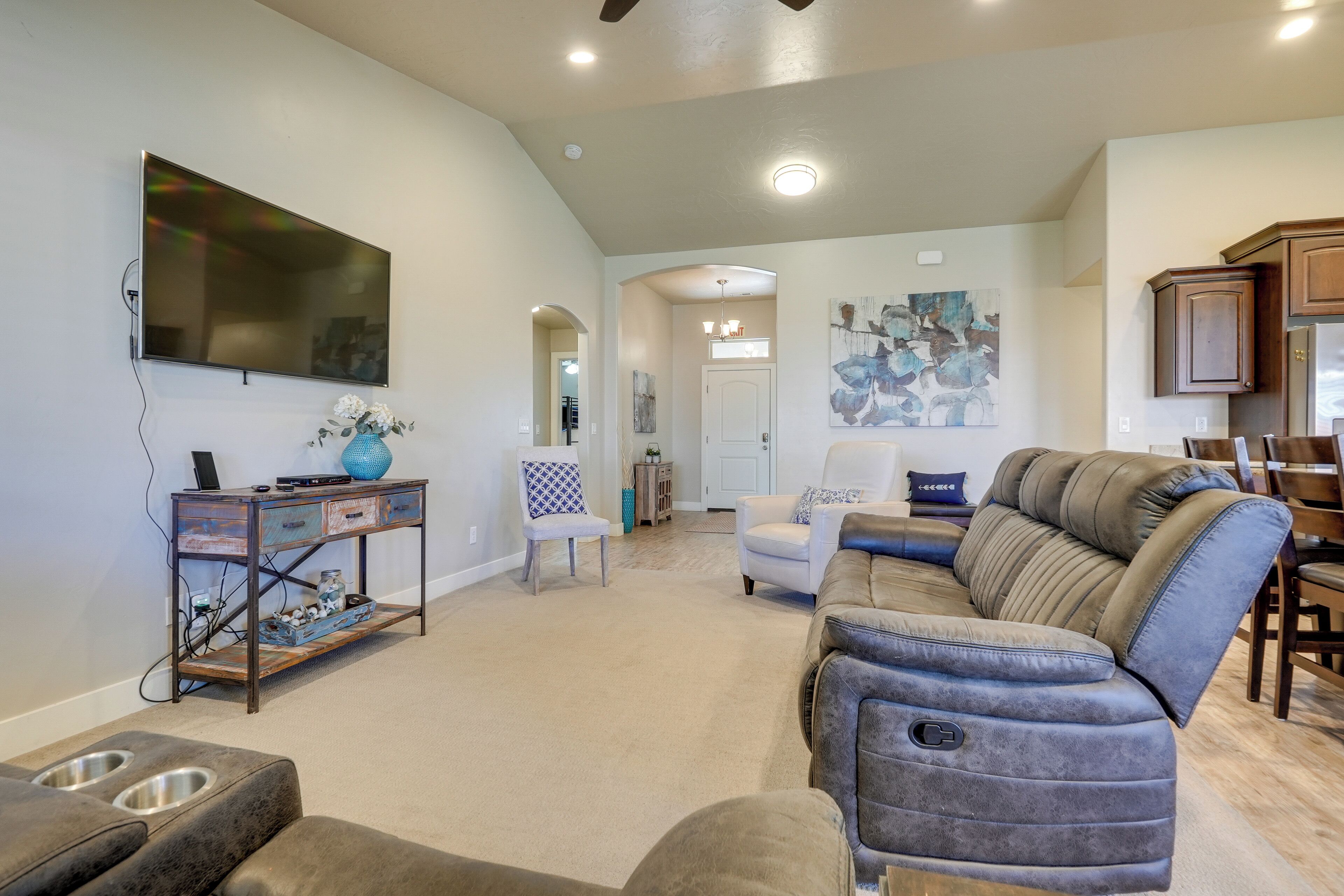A spacious living room with a large flat-screen TV, a comfortable sofa, a coffee table, and a dining area with wooden cabinets.