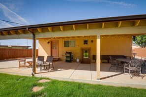 A covered patio area with outdoor furniture, a grill, and a door leading to the house. - Pet-friendly Kanab Getaway w/ Patio & Grill! (Kanab)