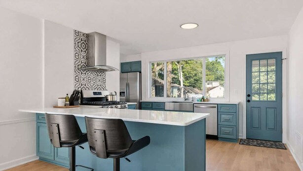 A modern kitchen with a central island, bar stools, a stainless steel range, and a teal color scheme.