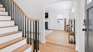 A staircase with wooden steps and black railings, leading to a living area with a fireplace, a white wall, and a door on the right.