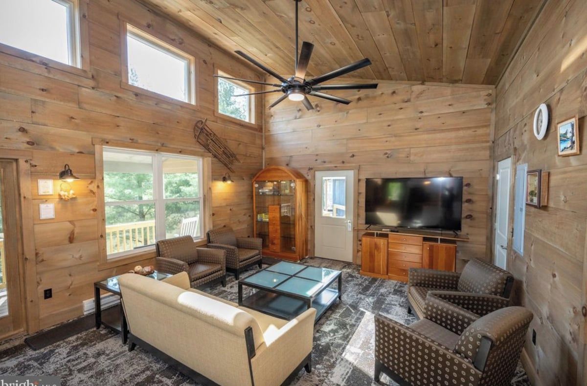 A log cabin interior with a sofa, chairs, a television, and a ceiling fan.