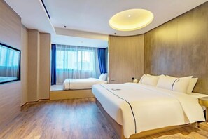 Ein Hotelzimmer mit einem großen Bett, einem kleineren Bett, einem Nachttisch, einem Fenster und einer Deckenleuchte.