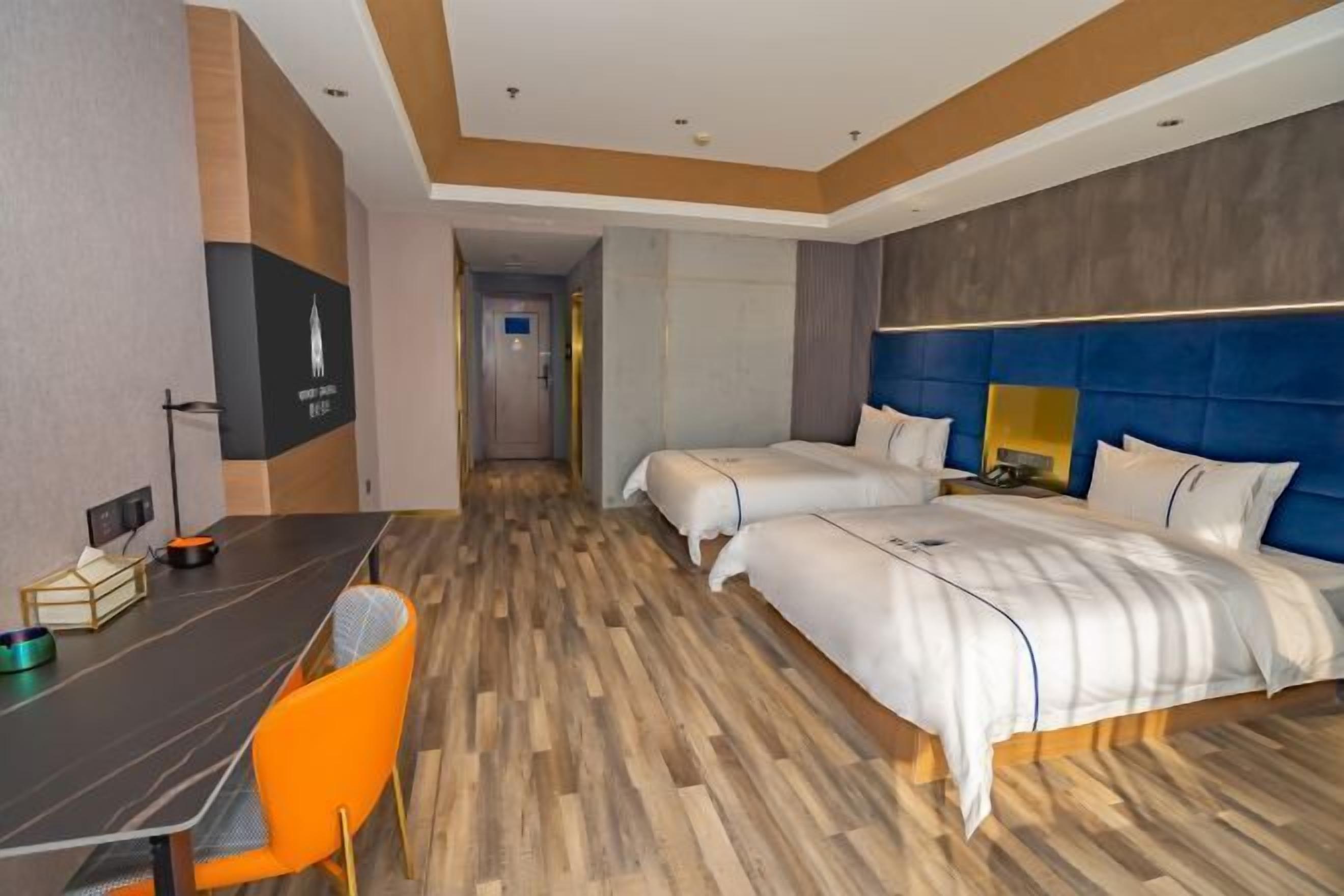 A hotel room with a bed, a desk, and a chair. There is a hallway leading to another room.