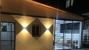 Ein modernes Gebäude mit gefliestem Patio, zwei Wandleuchten und einem großen Fenster mit Metallgitter.