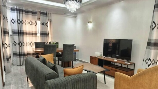 Ein modernes Wohnzimmer mit einer Couch, Sesseln, einem Couchtisch, einem Fernseher und einer Essecke mit Stühlen und Tisch.