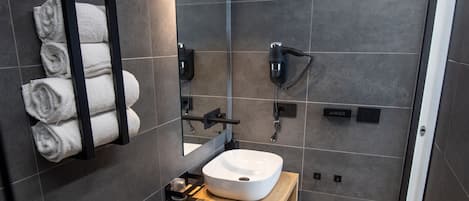 A modern bathroom with a white sink, a toilet, and a bidet. There are towels hanging on a rack, a mirror, and a hairdryer on the wall.