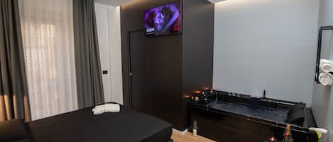 A modern hotel room with a large bed, a TV mounted on the wall, a small pool table, and a vase with flowers.