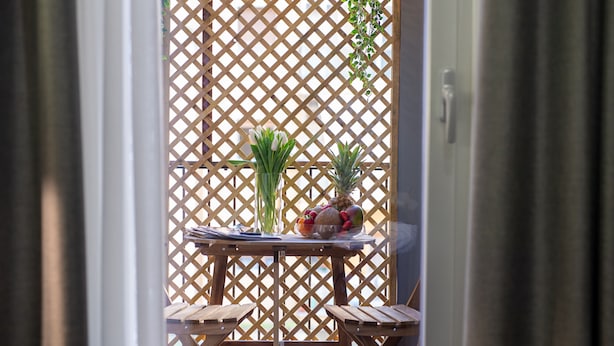 A wooden table with a fruit bowl and a vase of flowers, set against a lattice backdrop.