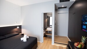 A modern hotel room with a bed, bedside table, and a TV mounted on the wall.