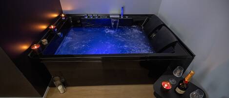 Un moderno spa con una bañera negra, velas y una botella de champán.