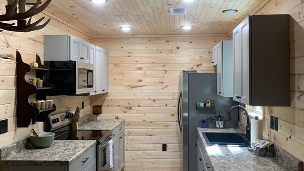 A narrow kitchen with wooden walls and ceiling, equipped with a microwave, stove, sink, and cabinets. - Cozy cabin in the woods.   Close to boat ramp.  Shared 5 bay boat storage  (Counce)