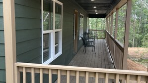 A covered wooden deck with a railing, a table with chairs, and a view of a forested area. - Cozy cabin in the woods.   Close to boat ramp.  Shared 5 bay boat storage  (Counce)