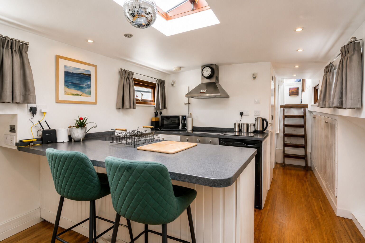 A modern kitchen with a central island, bar stools, a clock, and a skylight.