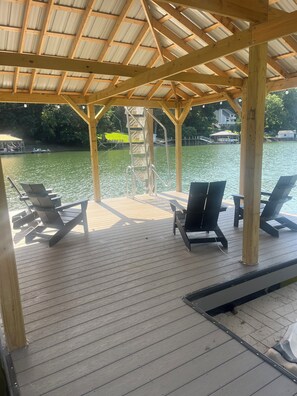 Eine Holzterrasse mit Liegestühlen und einer Metallleiter, mit Blick auf ein Gewässer mit einem Steg und Häusern im Hintergrund.