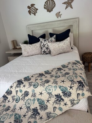 Ein Bett mit weißer Daunendecke, Kissen mit Sternenmuster, einer Wanddekoration in Form eines Seesterns und einem gewebten Korbletten.