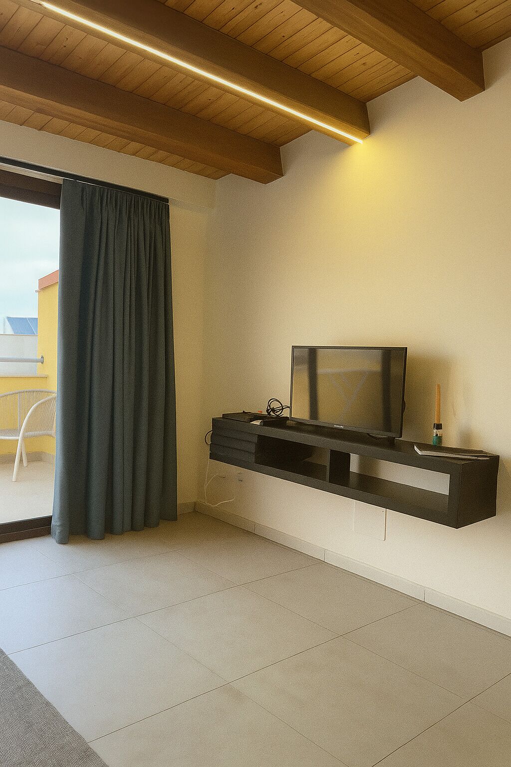 Een moderne woonkamer met een flatscreen televisie op een zwart tv-meubel, een groot raam met uitzicht op het omliggende landschap, en een houten plafond.