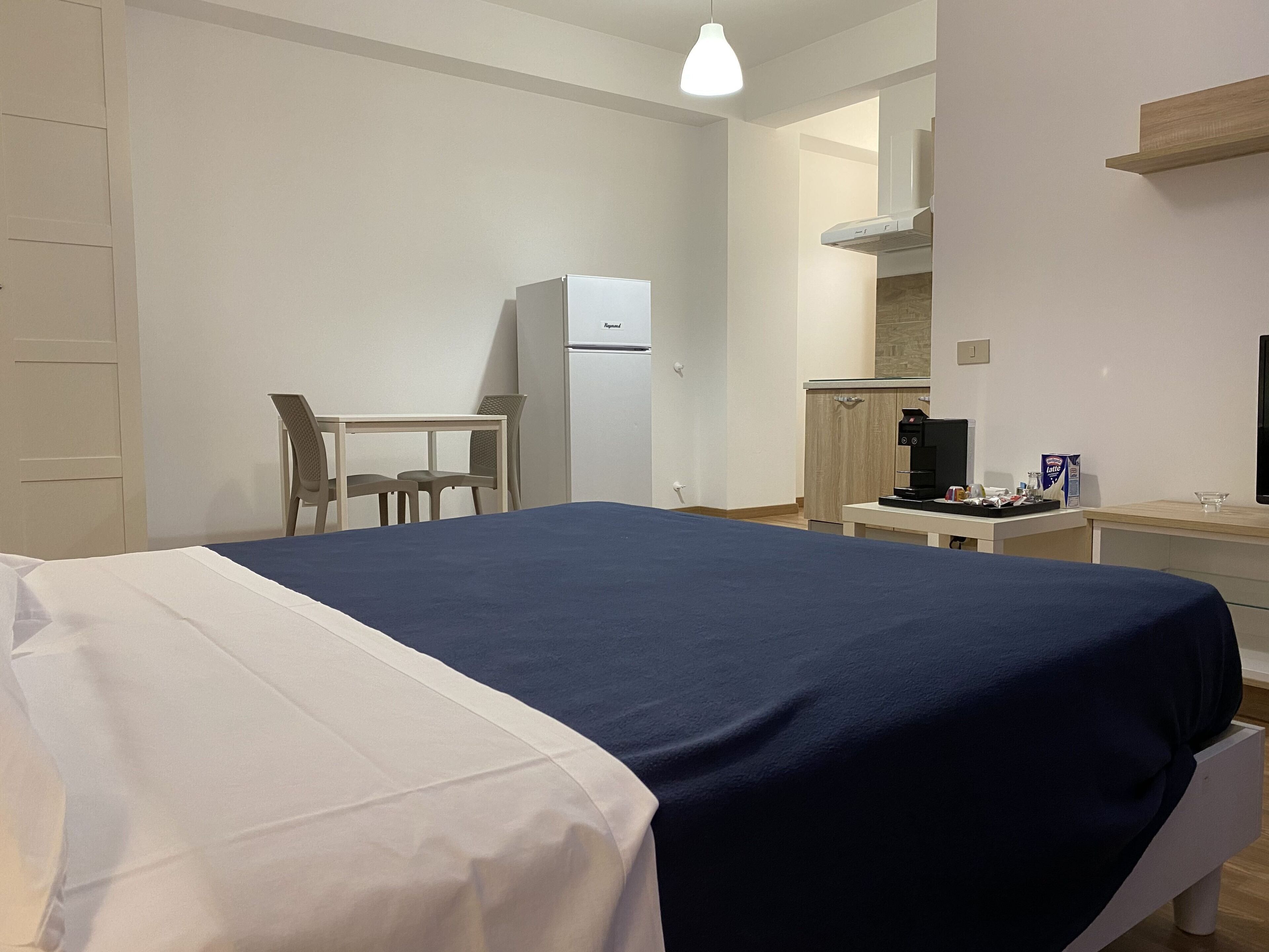 A hotel room with a bed, a desk, a refrigerator, and a coffee machine.