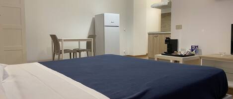A hotel room with a bed, a desk, a refrigerator, and a coffee machine.
