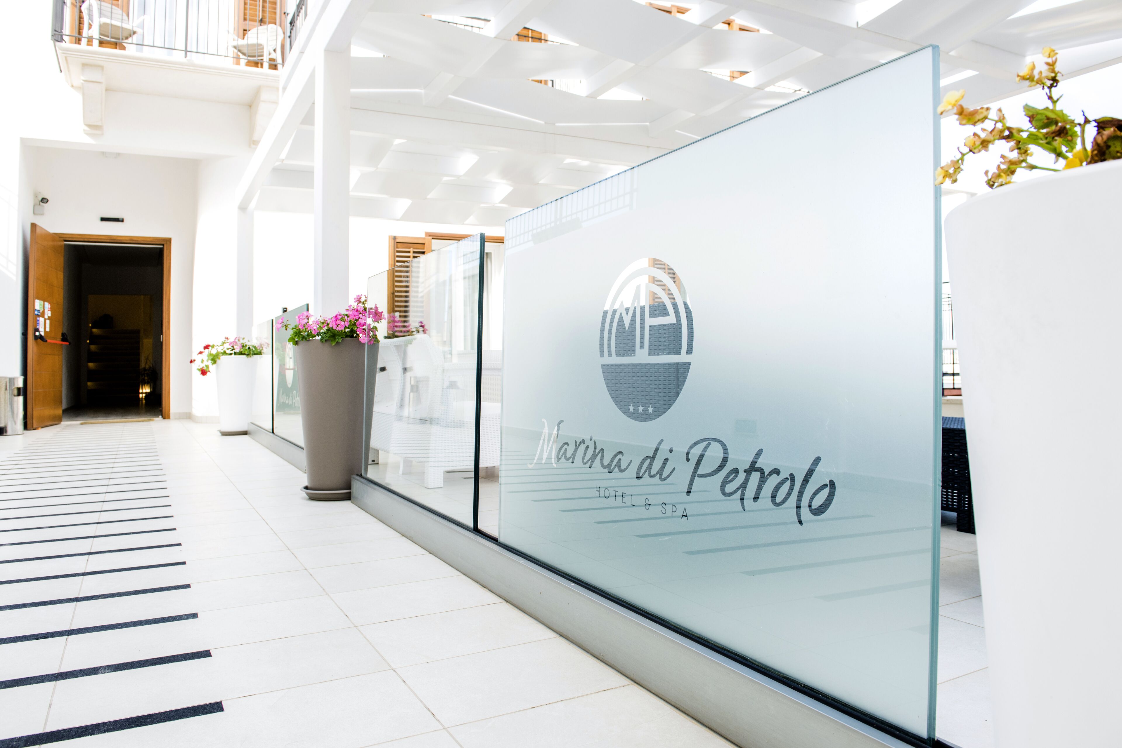Un corridoio moderno di un hotel con una parete di vetro che mostra il nome 'Marina di Pietrolo' e un logo.