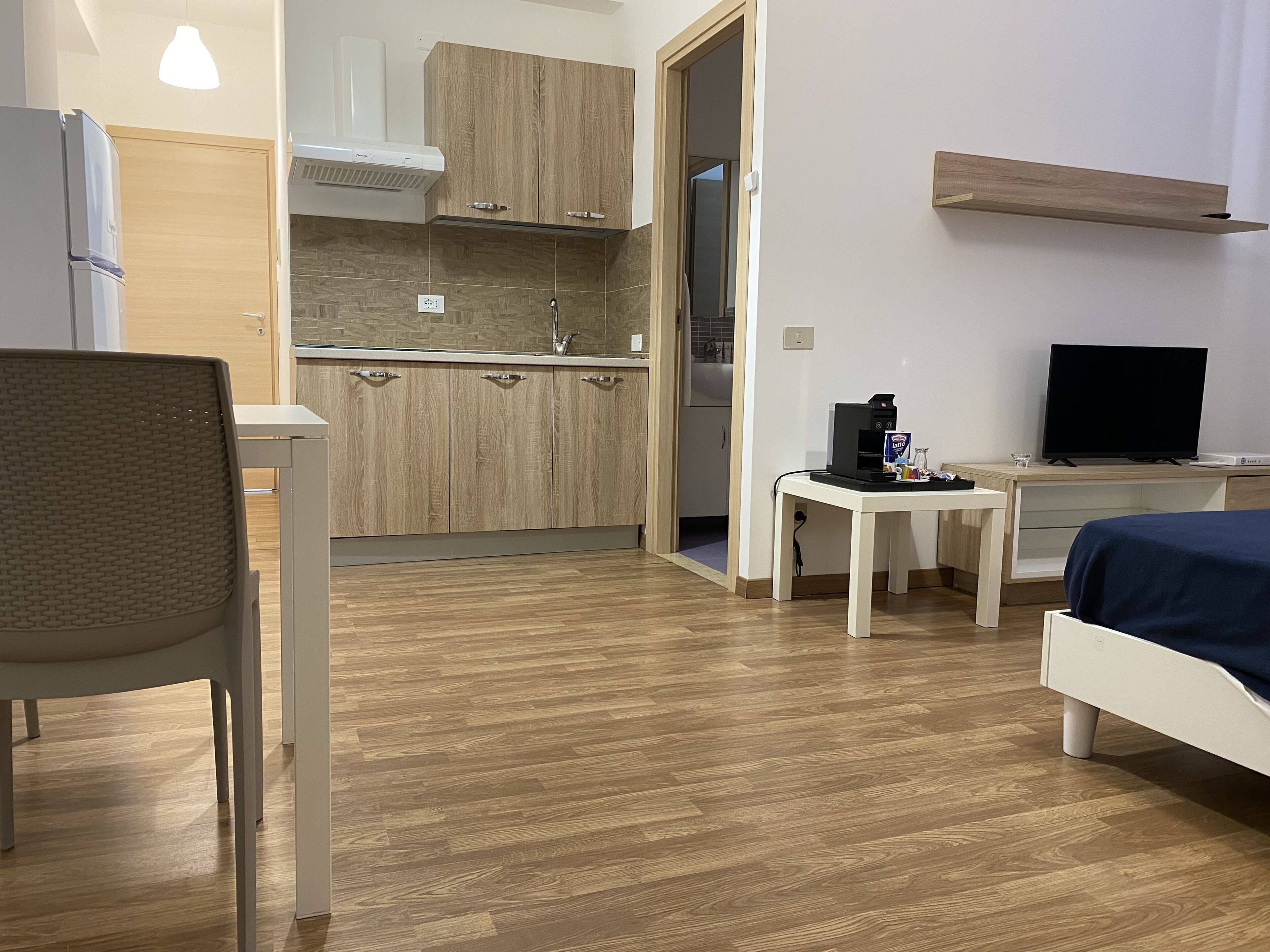 A compact hotel room with a kitchenette, a bed, a desk, and a TV.