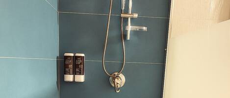 Un baño moderno con pared de azulejos azules, una ducha con cabezal de ducha manual y dos botellas de champú y acondicionador en la pared.