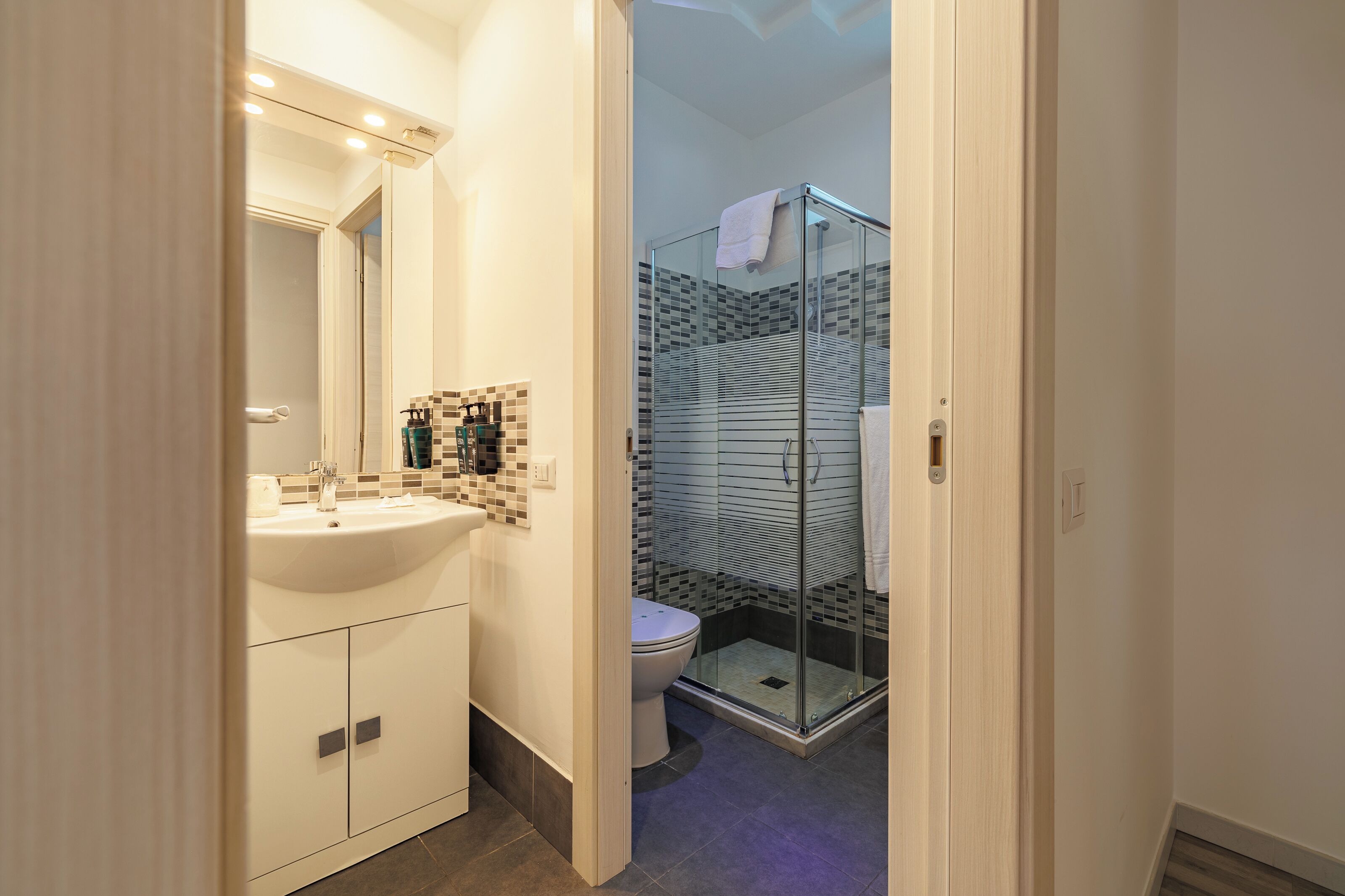 Een badkamer met een witte wastafel, spiegel en betegelde douchehoek.