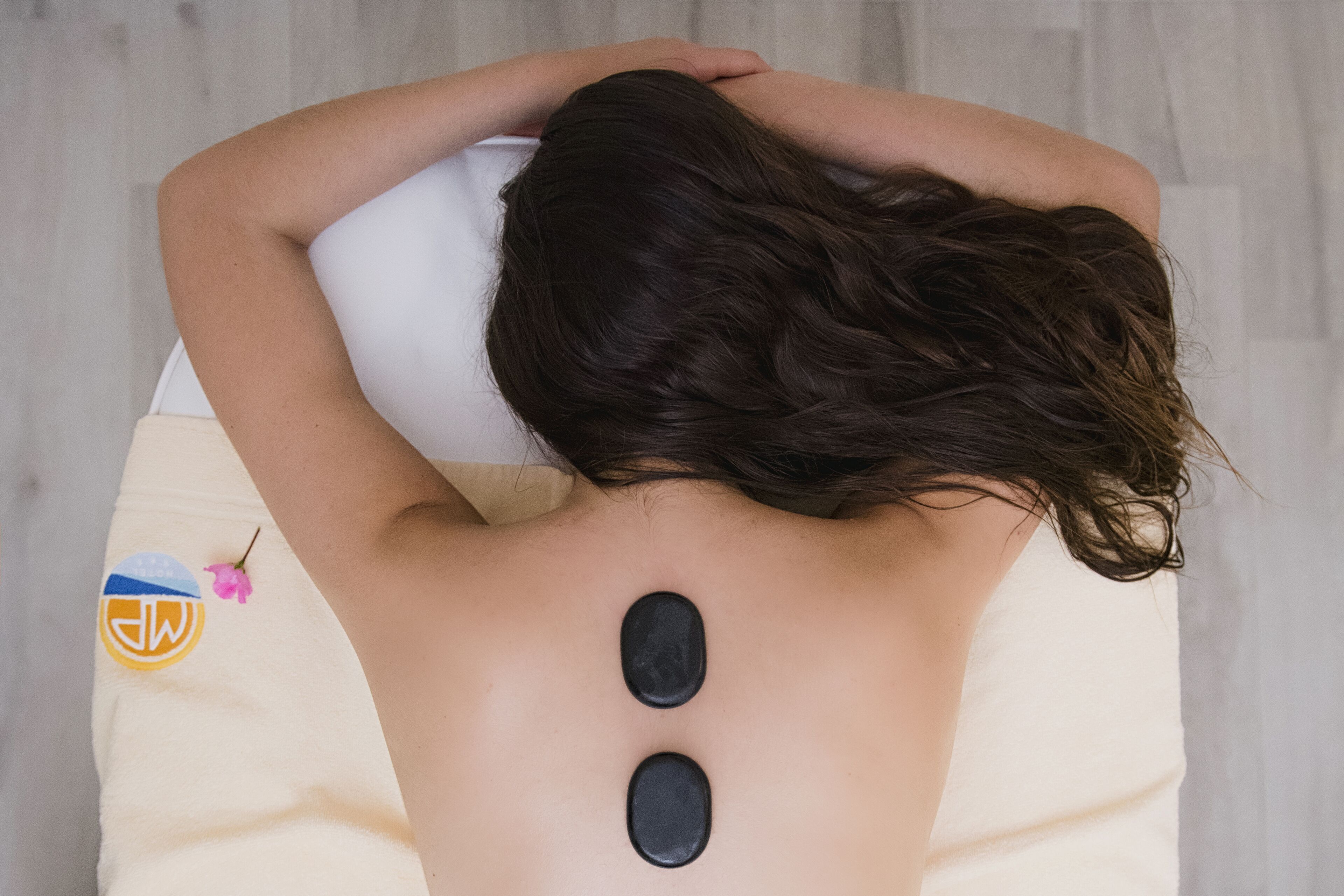 A person receiving a back treatment with two black stones on their back.