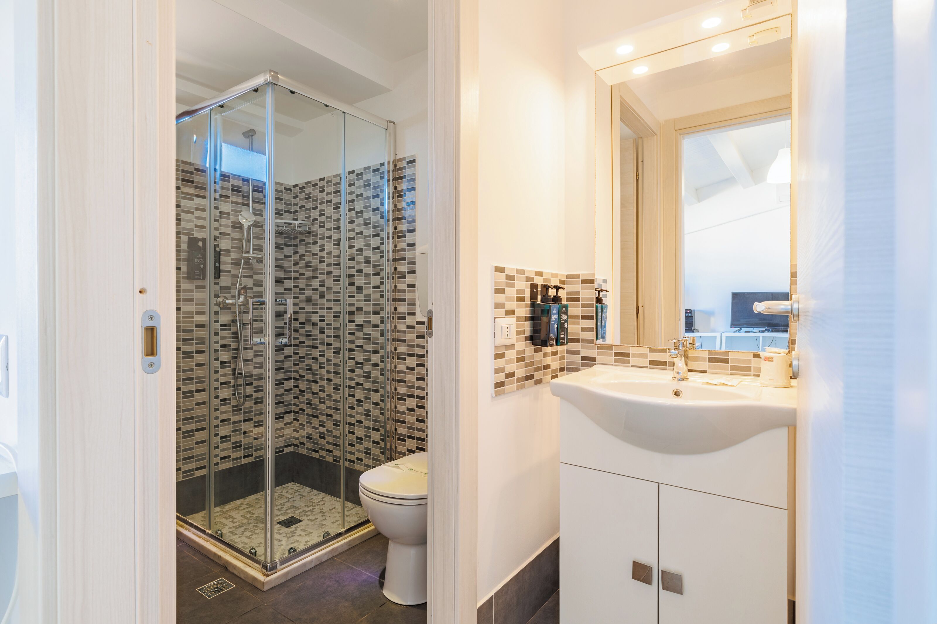 Un baño moderno con cabina de ducha de vidrio, inodoro blanco y lavamanos con salpicadero de azulejos.