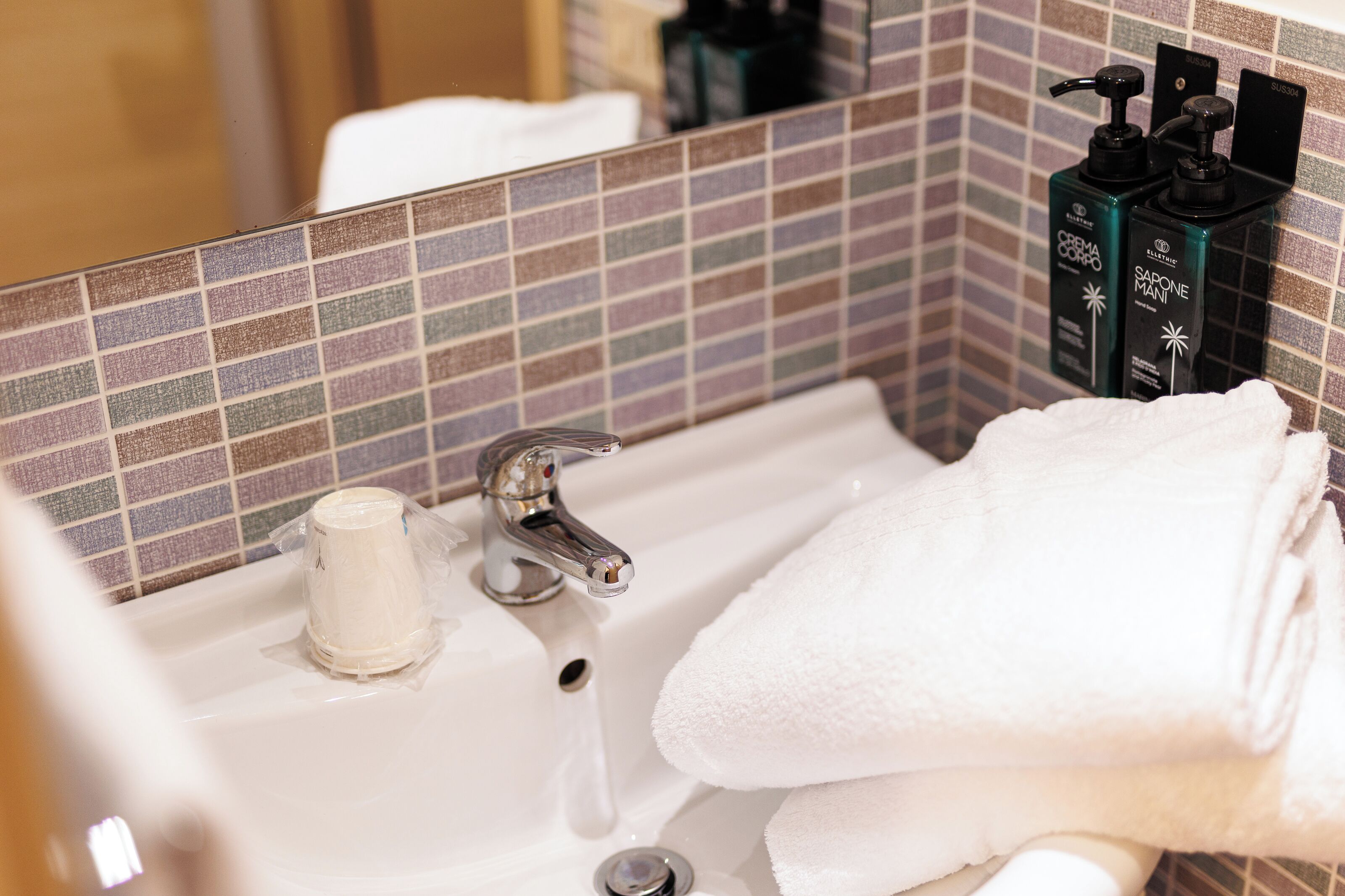 A bathroom with a tiled backsplash, a sink with a faucet, and toiletries on the wall.