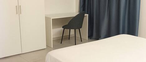 A bedroom with a bed, a desk, and a chair.