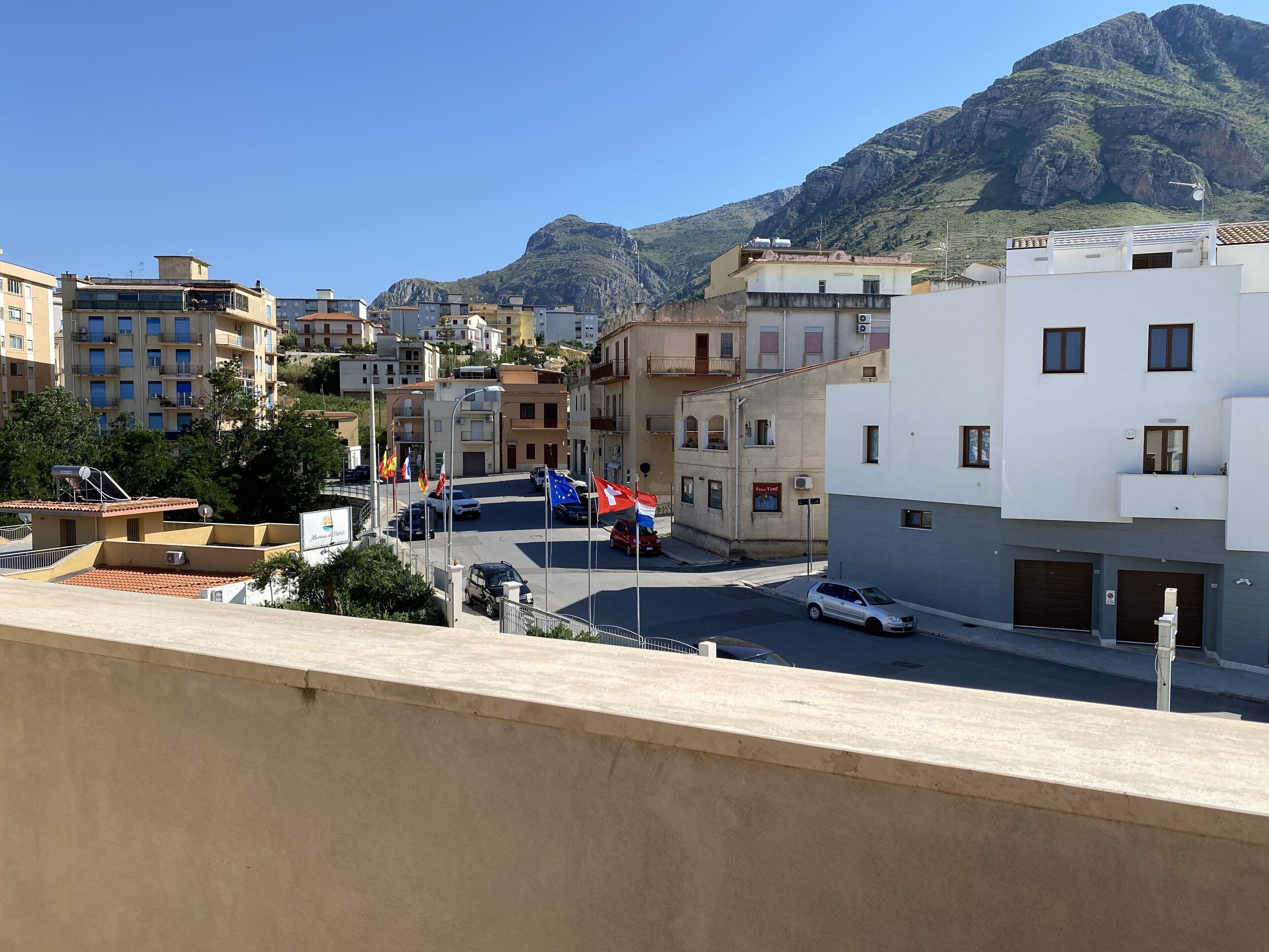 A residential street with buildings, a mountain in the background, and parked cars.
