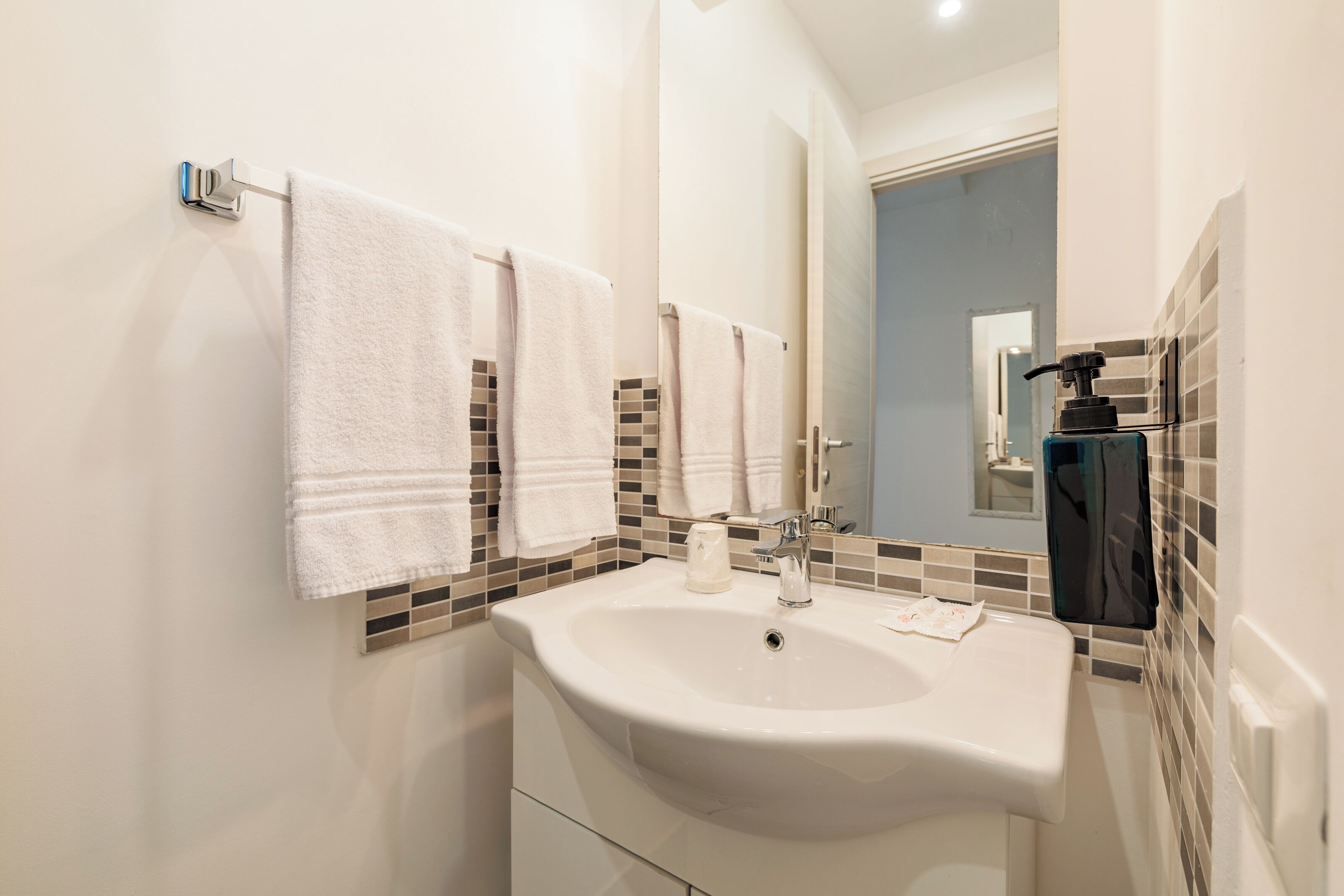 A bathroom with a white sink, a mirror, and two towels hanging on a rack.