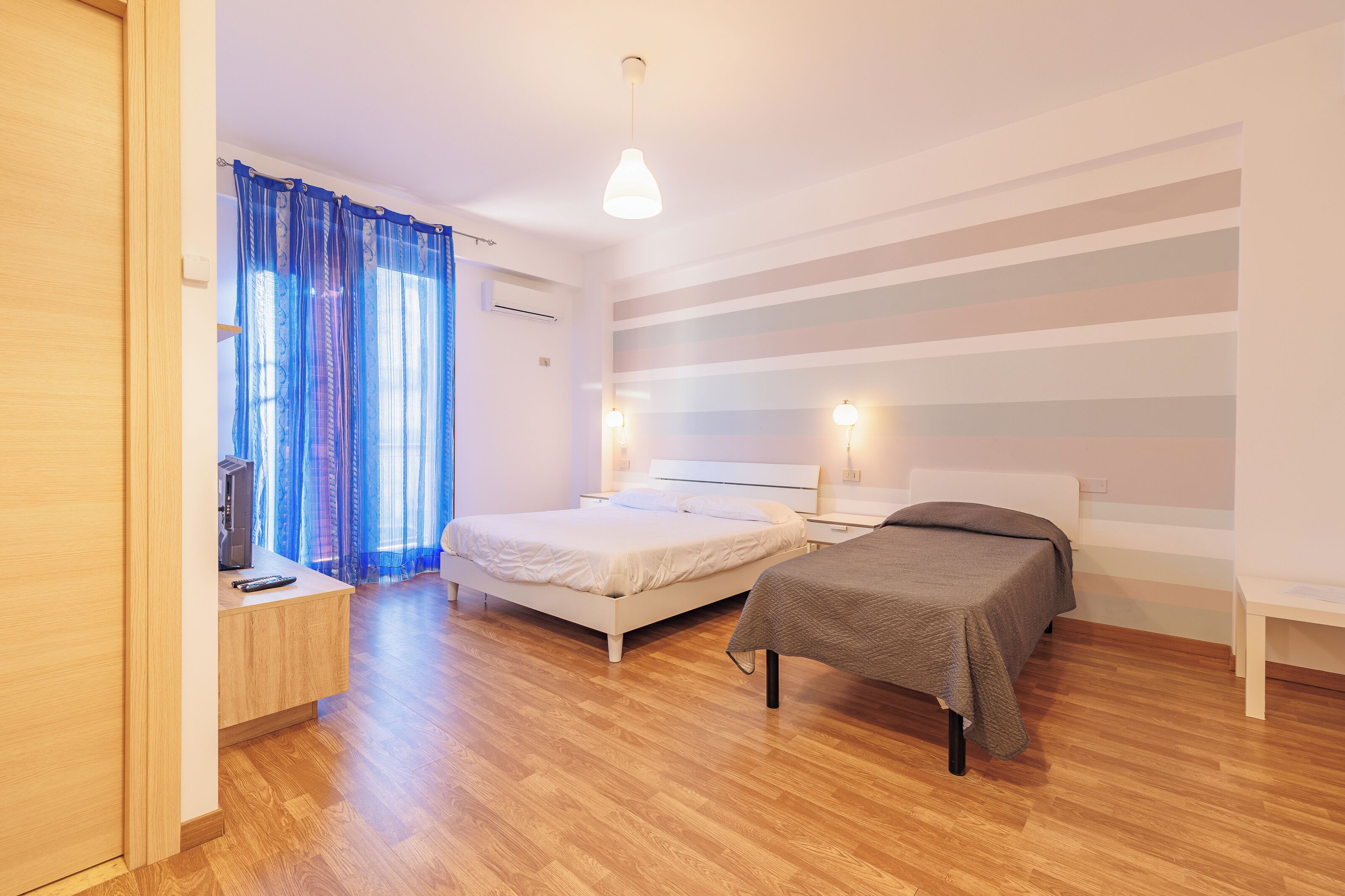 Un dormitorio con cama, mesitas de noche, un escritorio y una ventana con cortinas.
