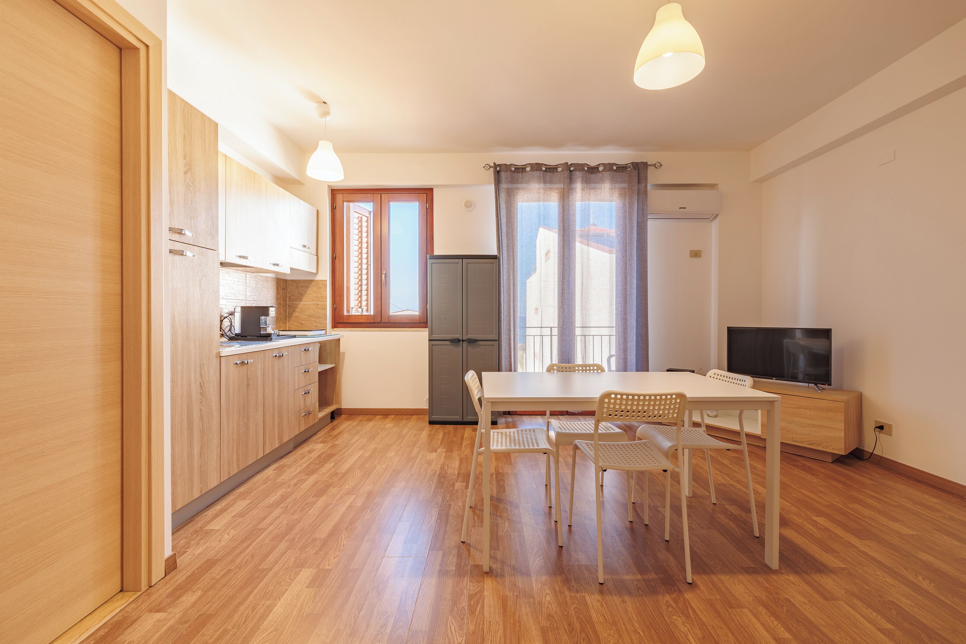 A compact kitchen with wooden cabinets, a dining table with chairs, a refrigerator, and a television.