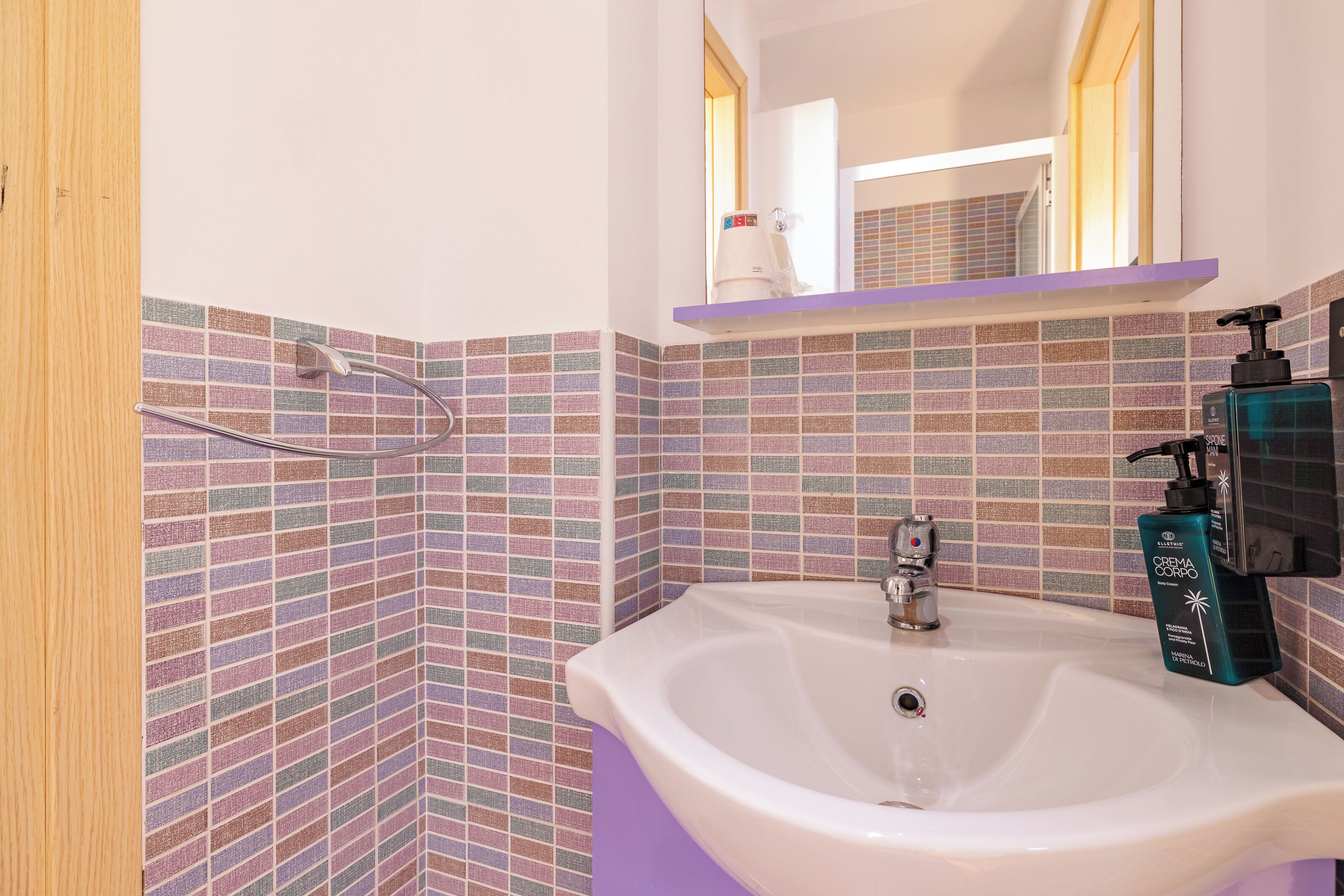 A bathroom with a white sink, a mirror, and a shelf with toiletries.