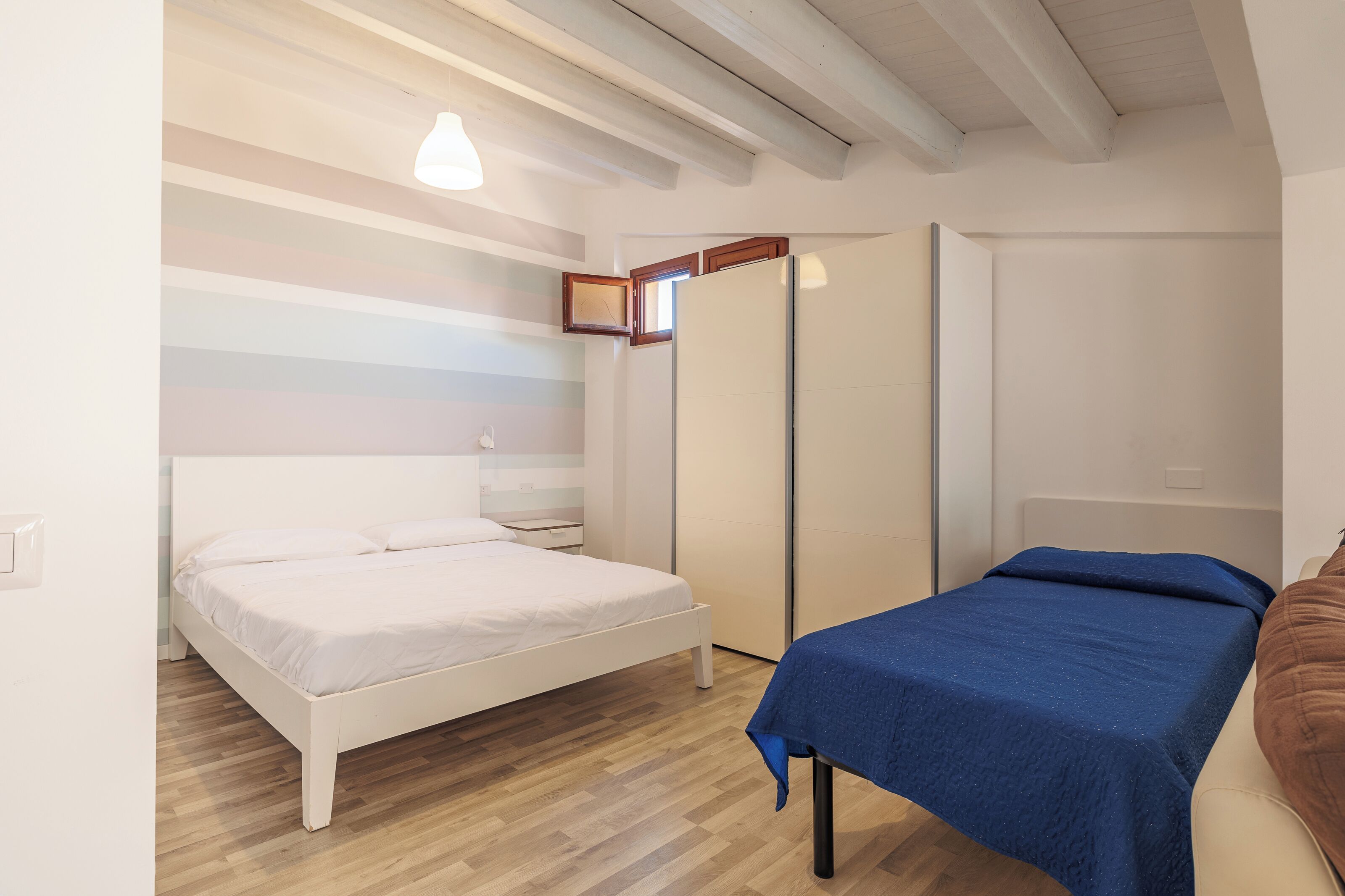 Een slaapkamer met een bed, nachtkastje, kledingkast en een kleintje tafeltje met een blauwe tafelkleed.