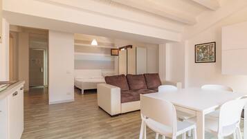 Una sala de estar moderna con un sofá blanco, una mesa de comedor con sillas y una zona de cocina con un refrigerador.