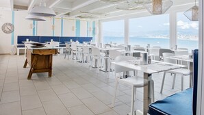 A spacious dining area with white tables and chairs, a wooden table, and hanging light fixtures. - Marina di Petrolo Apartments (Castellammare del Golfo)