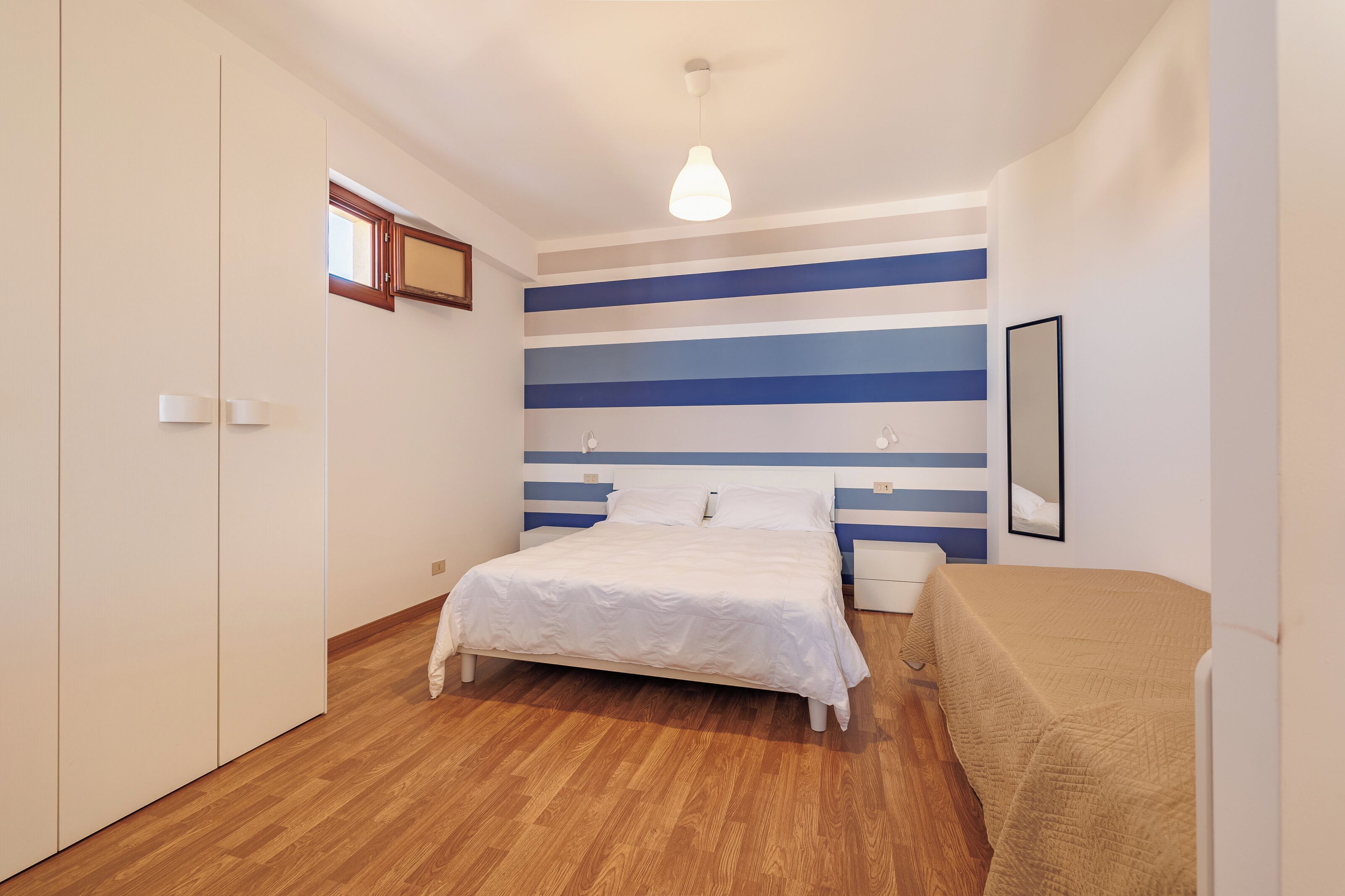 A bedroom with a bed, bedside tables, a wardrobe, and a striped wall.