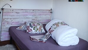 A bedroom with a wooden headboard, a heart-shaped wall decoration, a hanging light fixture, and a floral painting.