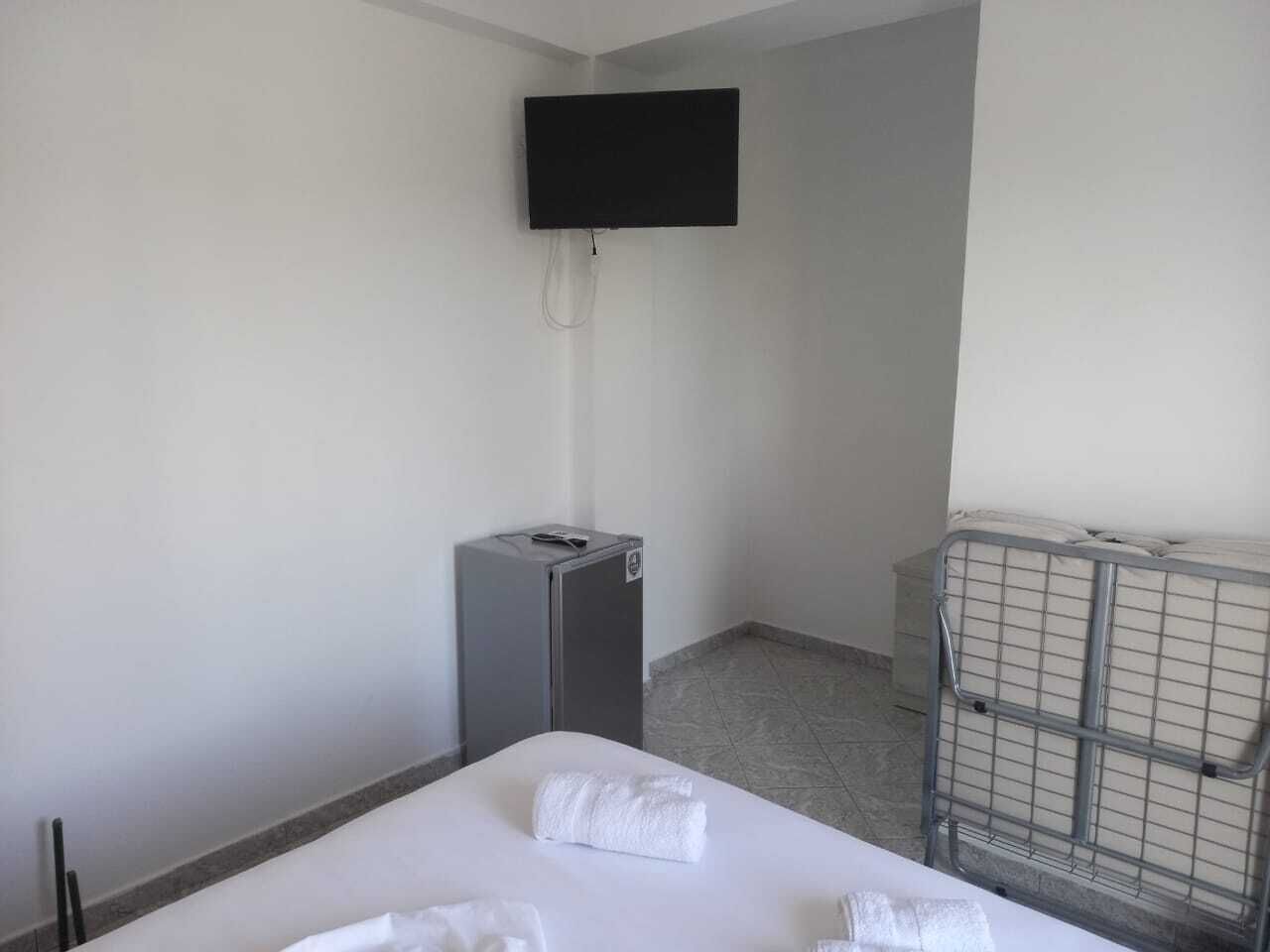 A hotel room with a bed, a small desk, a television mounted on the wall, and a metal bed frame.