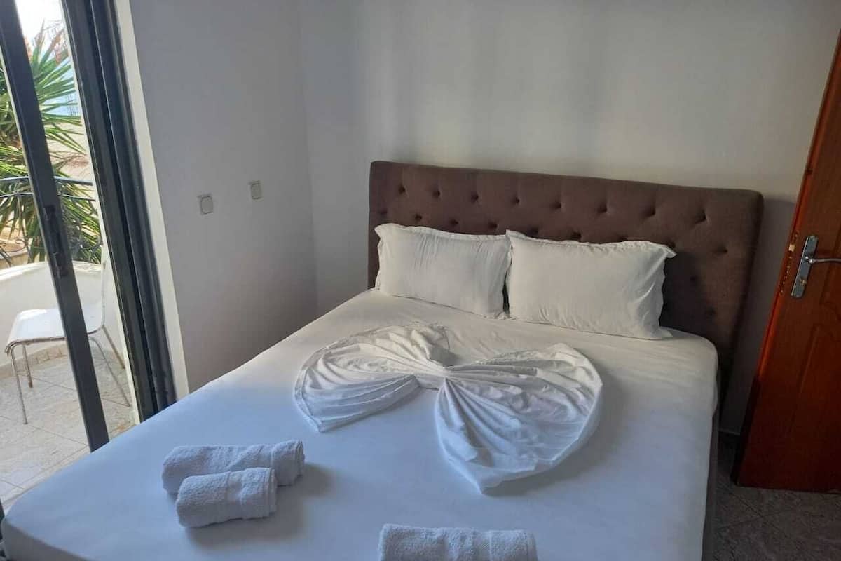 A neatly made bed with a large, decorative towel arrangement in the center, a wooden headboard, and a view of the outside through a glass door.
