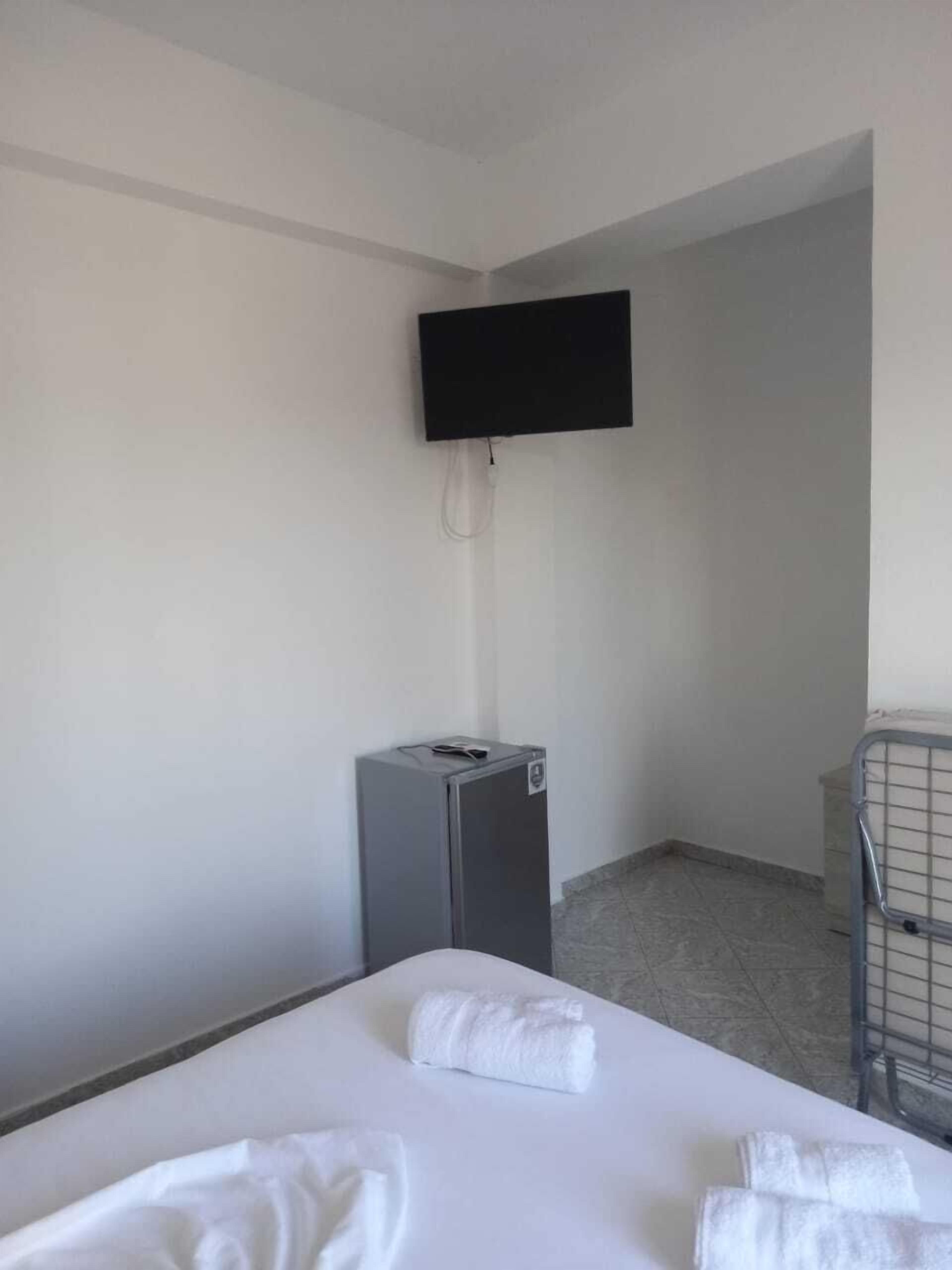 Une chambre d’hôtel équipée d’un lit, d’un téléviseur à écran plat fixé au mur, d’un petit réfrigérateur et d’une rambarde en métal.