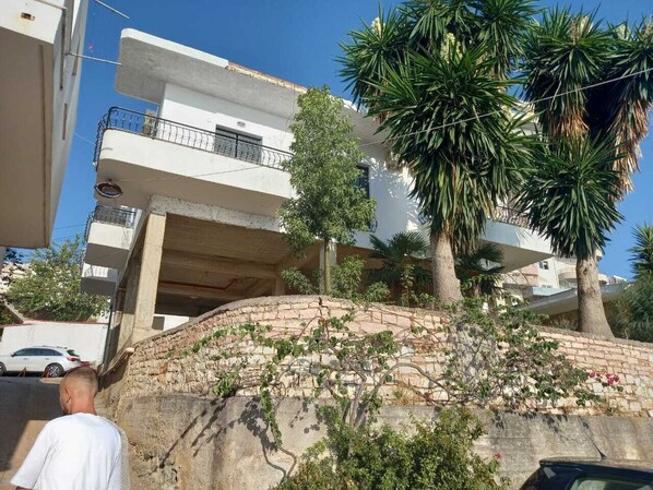 Ein Wohngebäude mit Balkon, Steinmauer und einer Palme.